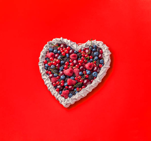 istock Berries overhead white heart shaped vibrant arrangement on red background 1196526740
