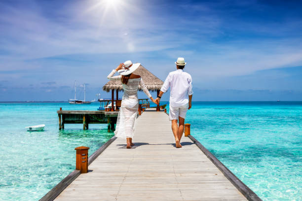 カップルはモルディブ、インド洋の熱帯の海の上に木製の桟橋に沿って歩きます - tree men nature human hand ストックフォトと画像