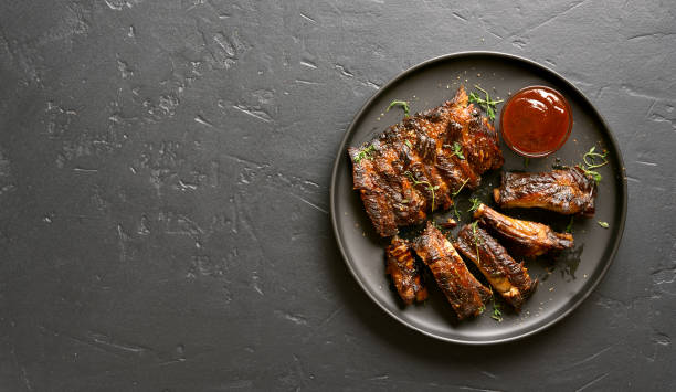 Grilled spare ribs Spicy hot grilled spare ribs on plate over black stone background with copy space. Tasty bbq meat. Top view, flat lay pork stock pictures, royalty-free photos & images
