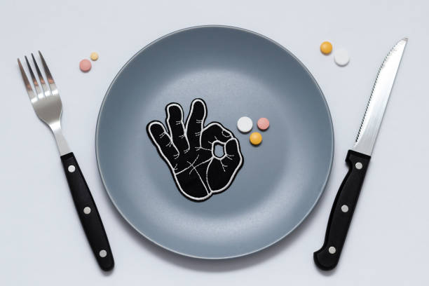 istock Multicolored pills and okay symbol on a gray plate next to a knife and fork on a white background. Medical concept. 1196530231