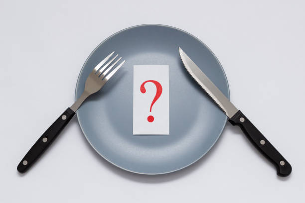 istock Red question mark on a gray plate next to a knife and fork on a white background. Medical concept. Diet. 1196530267