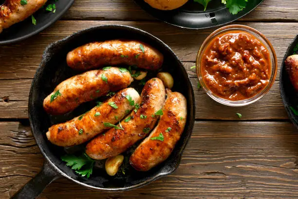 Fried sausages in frying pan over wooden background. Top view, flat lay