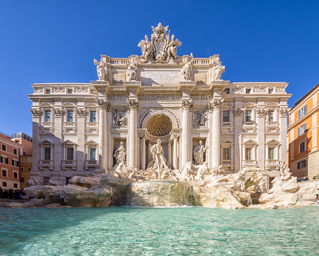 Trevi Fountain was built against the back of the Palazzo Poli building. In the centre underneath the arch stands the statue of the nautical god Neptune, being pulled to the sea on his shell-shaped chariot pulled by two winged horses and tritons. One of the horses is calm and obedient, the other is boisterous. They symbolise the changing tides of the sea. The two statues in the niches (made by Filippo della Valle) next to Neptune represent Abundance to the left and Health to the right.