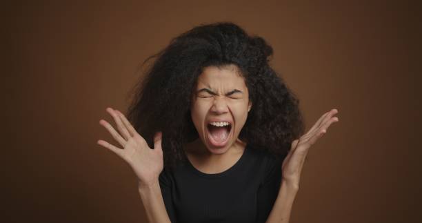 Portrait of african american girl shouting against the brown wall background Portrait of african american girl shouting against the brown wall background. slow motion face stock pictures, royalty-free photos & images