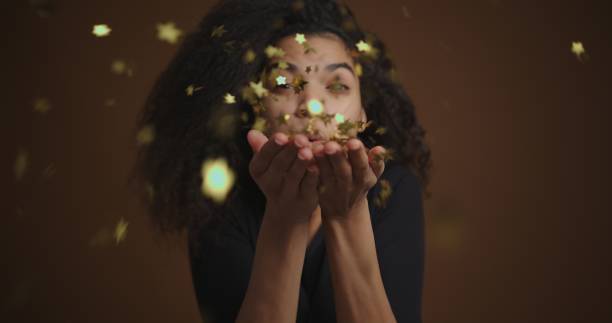 Close up african american girl blowing gold glitter off hands to camera Close up african american girl blowing gold glitter off hands to camera. slow motion face stock pictures, royalty-free photos & images
