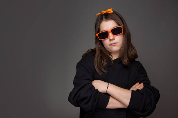 teenage girl with arms folded orange glasses hair bow black sweatshirt on a gray background stock photo
