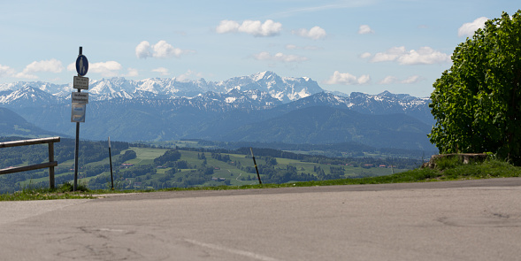 PEISSENBERG, BAVARIA / GERMANY - June 2, 2019: Panorama view of Wetterstein mountain range. In the middle Zugspitze, Germanys highest mountain, The mountains are framed by a sign post and bushes.