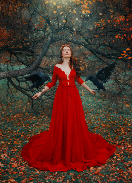 istock attractive redhead witch queen red dress with deep neckline. Two wise ravens on arms. Magic sun rays shine energy radiance and sparkles of blessing poured on woman from sky. calmfortune telling 1196546716