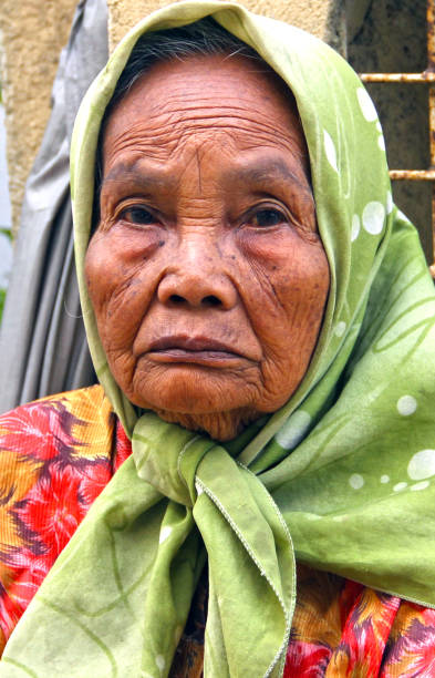 An elderly Asian woman looking at the camera with a smile while sitting on a chair on a white background