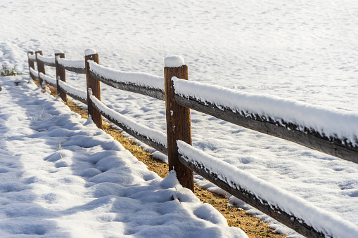 Long wooden post fence with ground covered snow.