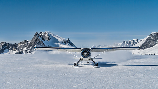 A scale model of a bare-metal DC-3 Dakota in flight, flying high above the snow-capped peaks of a mountain range.