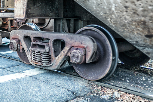 Close-up of a moving freight train railroad box freight car wheels and the supporting wheelset and chassis assembly. Shot taken as the wheels are crossing through a road intersection on old, well-worn steel railroad tracks. These wheelset assemblies are called either \