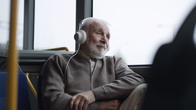 Senior man listening music on headphones in bus