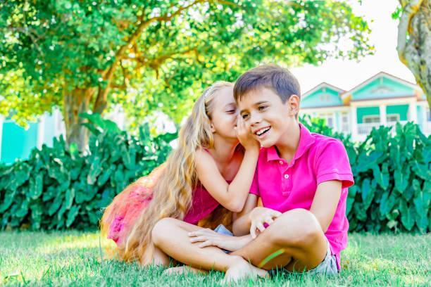 a menina que sussurra um gracejo na orelha de um menino, menino está rindo, fundo do jardim do verão - whispering couple discussion smiling - fotografias e filmes do acervo