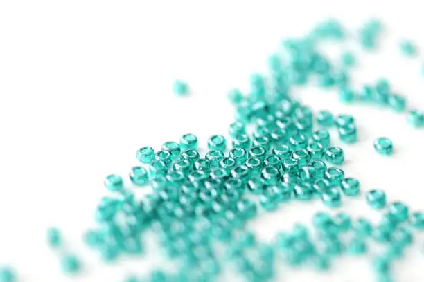 Transparent seed beads aquamarine color scattered on a white surface close-up