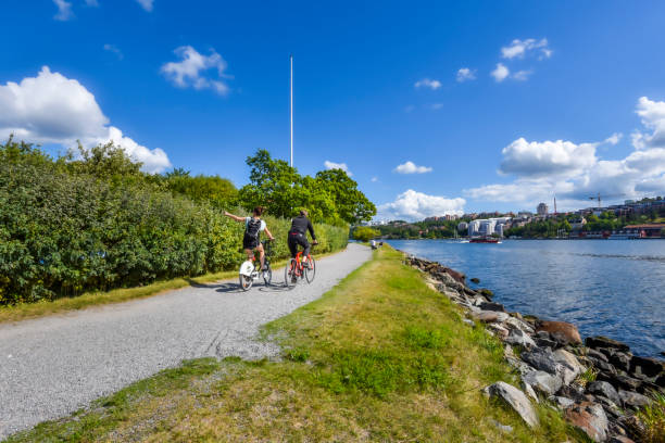 Cyclist on the water face promenade in Djurgarden island in Center of Stockholm. Waters of Saltsjon bay is at right. Stockholm, Sweden  August 18, 2017 Cyclist on the water face promenade in Djurgarden island in Center of Stockholm. Waters of Saltsjon bay is at right. djurgarden photos stock pictures, royalty-free photos & images