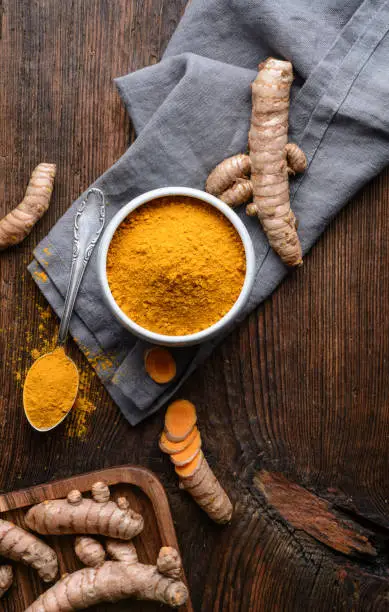 Anti-inflammatory food ingredient, turmeric powder in a ceramic bowl and fresh root on rustic wooden background