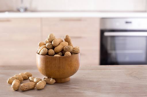 Heap of peanuts in shell in bowl standing on table with kitchen in background