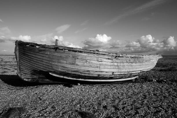 Fishing Boat at Dungeness.  Black and white image taken with a wide angle lens. Monochrome landscape image taken on the beach. Abandoned side view of a boat in a barren landscape.