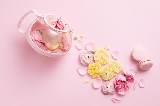 Top view of creative layout of pink teapot and tea cup with flowers on pink background.