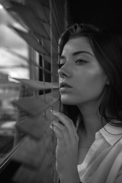 istock Girl looks through blinds 1196666781