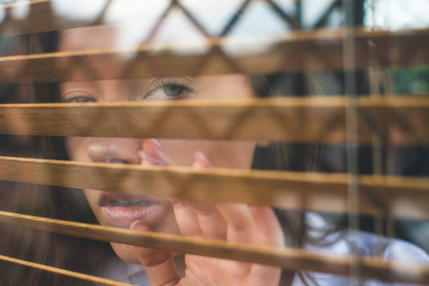 istock Girl looks through blinds 1196666900