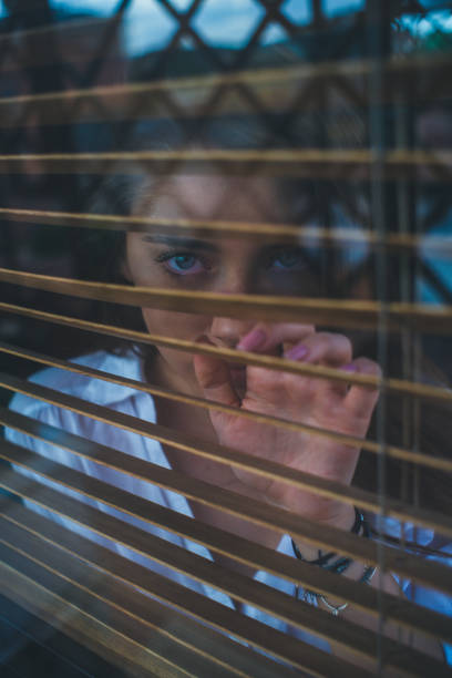 istock Girl looks through blinds 1196667035