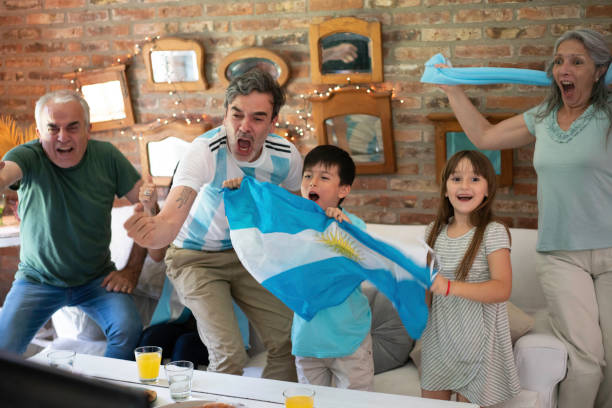 aficionados de fútbol familiar argentinos alegres, gritando comiendo pizza para llevar y mirando juego de fútbol - argentina mundial fotografías e imágenes de stock