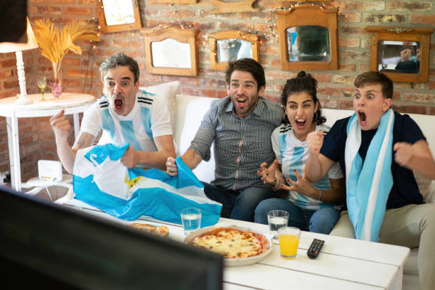 Argentinian soccer fans  cheerful, screaming eating takeaway pizza  and looking soccer play Argentinian cheerful group of friends watching football game on tv, having fun at home. argentinian culture stock pictures, royalty-free photos & images