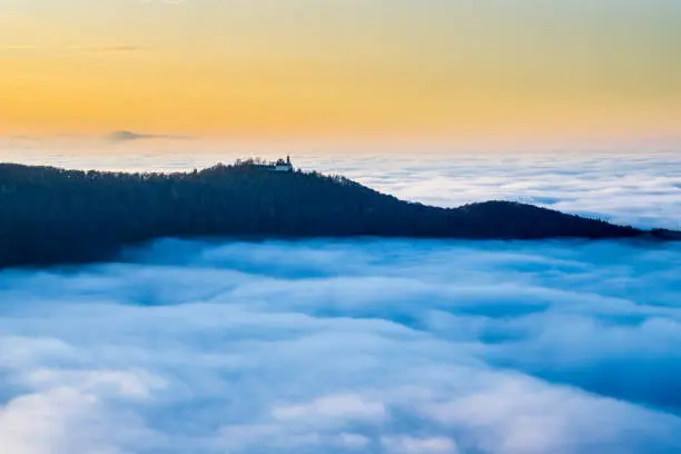 Germany, Magical aerial view above foggy cloudscape in the valley of Swabian Jura nature landscape at sunset with orange sky near Stuttgart