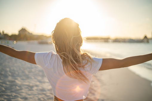 Joven alegre abrazando la naturaleza al atardecer; mujer de pie en los brazos de la playa extendido photo