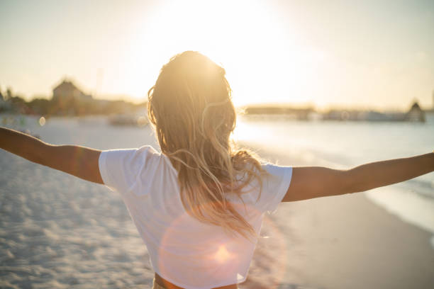 allegra giovane donna che abbraccia la natura al tramonto; femmina in piedi sulle braccia della spiaggia disteso - medicina alternativa foto e immagini stock