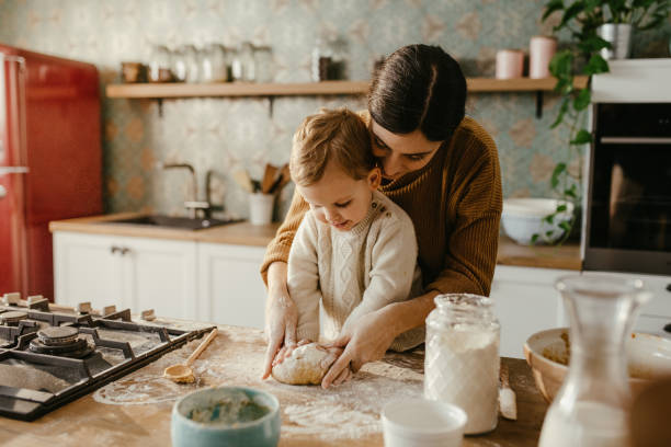 Mother and son making cookies Young mother and little son are making dough for cookies together. They are happy and mother is overseeing him. They wear casual winter clothes. slovenia photos stock pictures, royalty-free photos & images