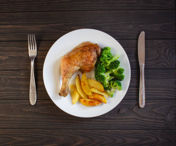 Roasted chicken legs served with potatoes and broccoli pictured from above. Top view.