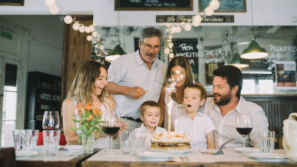 Celebration concept. Family celebrating child’s birthday in a restaurant. Boy blowing out the candle on a cake.