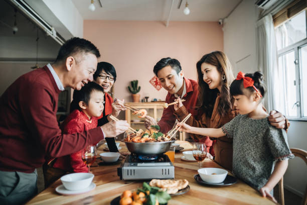 Three generations of joyful Asian family celebrating Chinese New Year and enjoying traditional Chinese poon choi on reunion dinner stock photo
