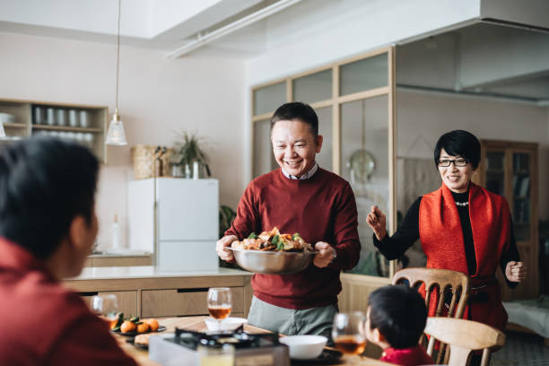 trois générations de famille asiatique joyeuse célébrant le nouvel an chinois et les grands-parents servant le poon choi chinois traditionnel sur le dîner de réunion - asian meal photos et images de collection