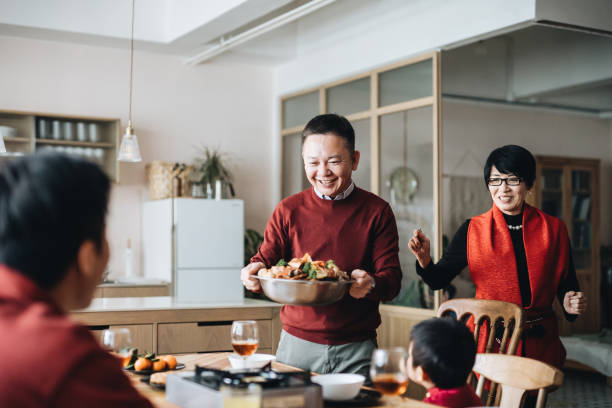 Three generations of joyful Asian family celebrating Chinese New Year and grandparents serving traditional Chinese poon choi on reunion dinner Three generations of joyful Asian family celebrating Chinese New Year and grandparents serving traditional Chinese poon choi on reunion dinner china chinese ethnicity smiling grandparent stock pictures, royalty-free photos & images