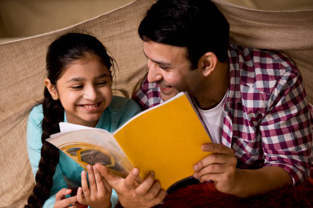 Father reading a book to his daughter under cover
