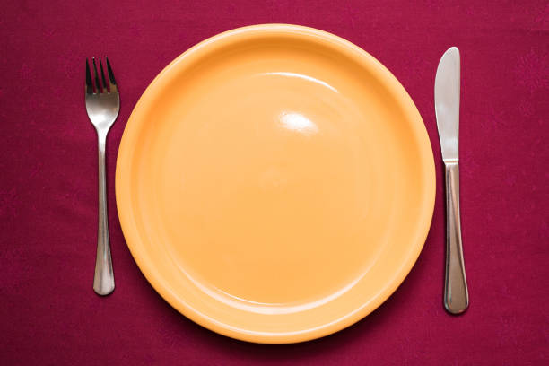 Empty yellow plate, fork and knife on maroon tablecloth. Elegant table setting. Top view, close-up