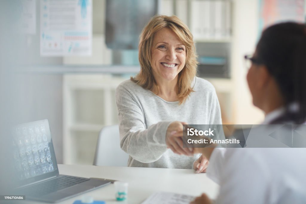 Patient visiting her doctor Mature happy patient sitting at the table and greeting with her doctor and smiling to her during her visit at clinic Doctor Stock Photo