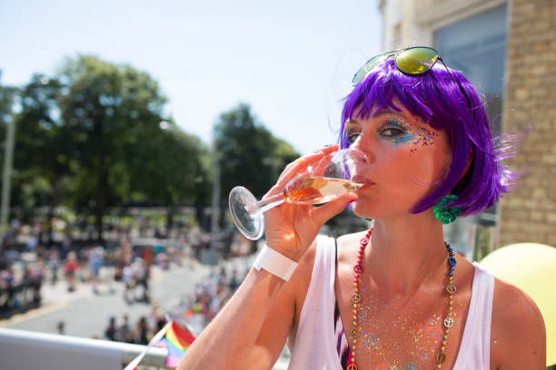 Pretty young woman at Gay Pride Pretty young woman wearing a purple wig and glitter make up while drinking champagne in the sunshine at Gay Pride Brighton. brighton england stock pictures, royalty-free photos & images