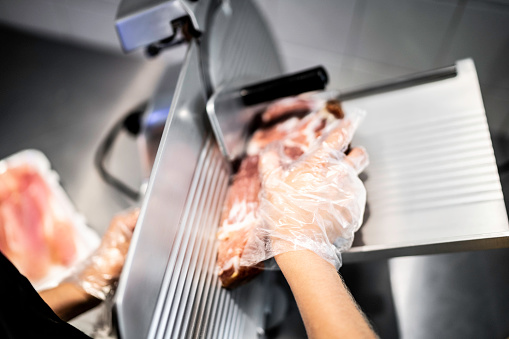 Human hand slicing a piece of ham in the meat slicer