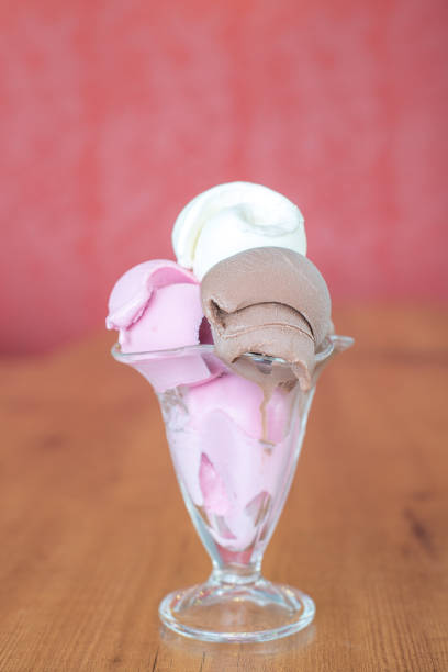 3 balls ice cream in the glass on the wooden table isolated background. This ice cream is chocolate strawberry and vanilla flavored