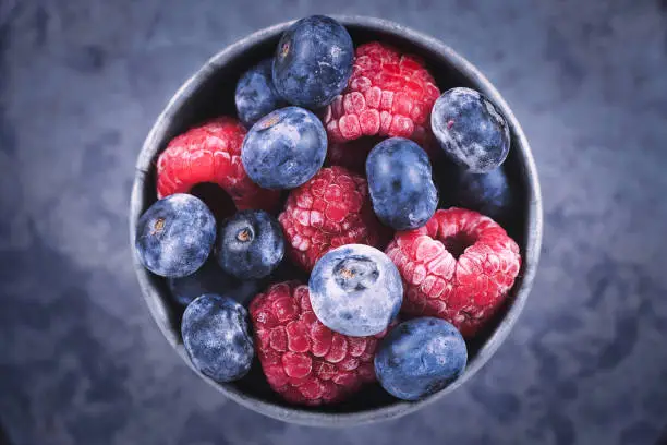 Photo of Top view of mixed blueberry and raspberry fruits in iron cup
