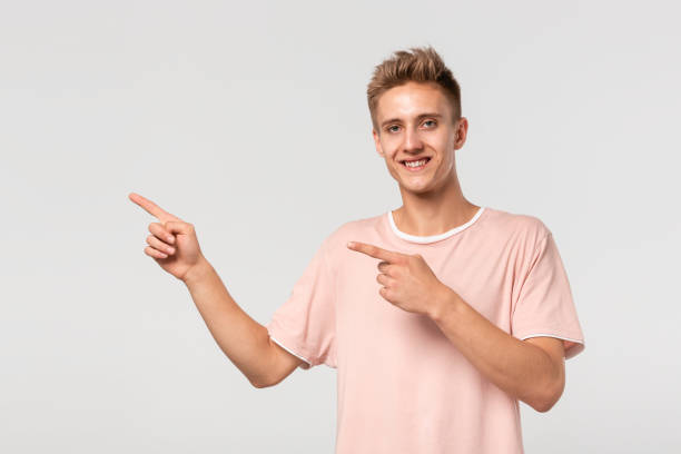 istock Handsome young man in a pink tee showing with his fingers left at the empty space for advertising. 1196728399