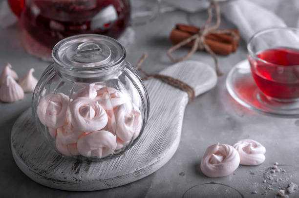 Small colorful meringues in the  glass jar on pink tile background