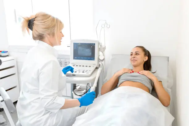 Photo of A gynecologist sets up an ultrasound machine to diagnose a patient who is lying on a couch. A transvaginal ultrasound scanner of the internal organs of the pelvis. Female health concept