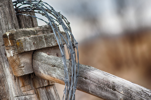 Barbed wire looped around an old rustic fence post with blurred background of an open field.