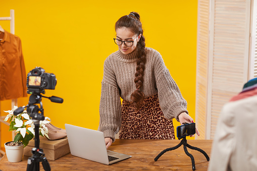 Portrait of contemporary young woman setting up cameras in studio while filming video for beauty and lifestyle channel, copy space